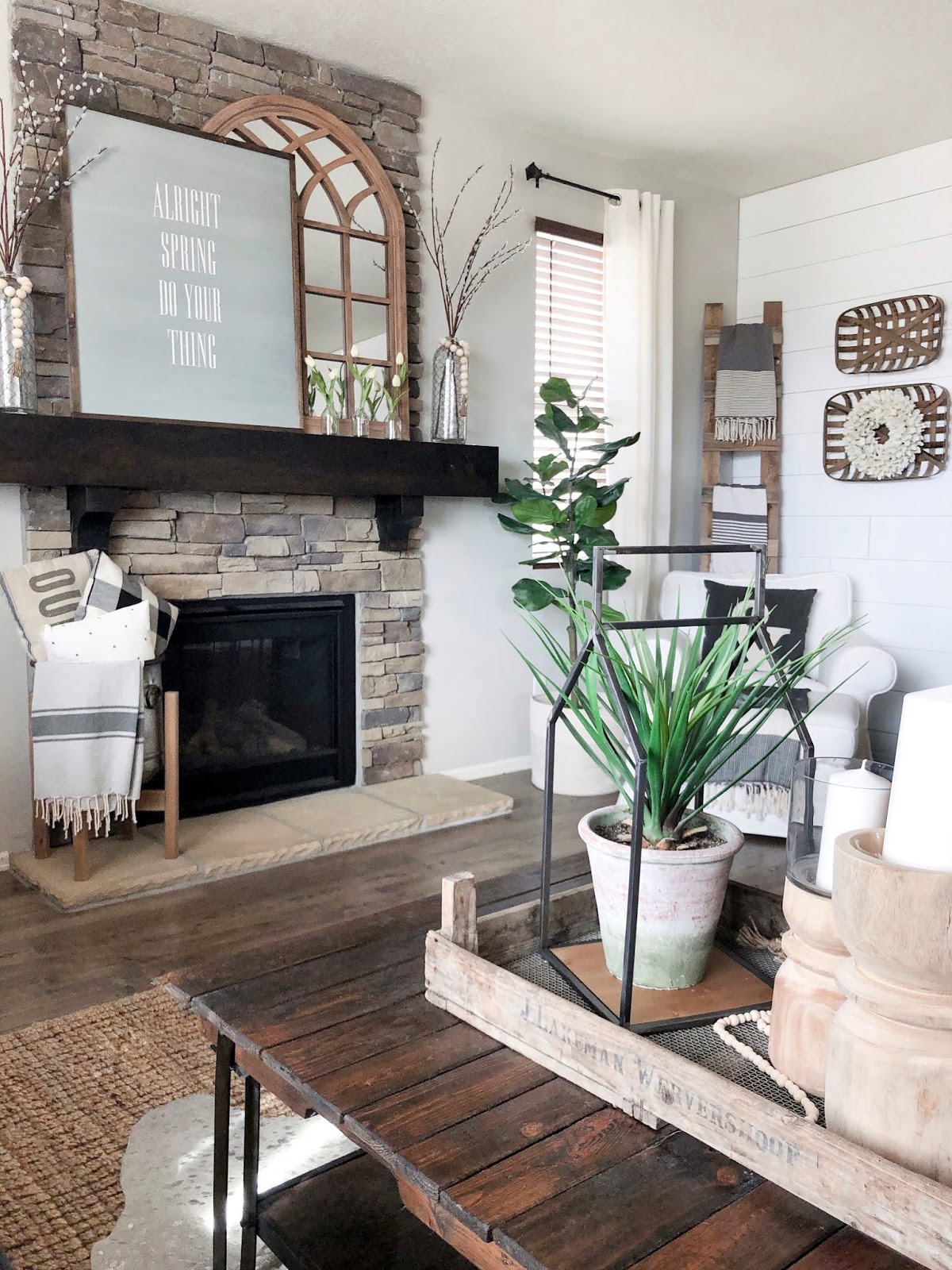 Spring farmhouse styled fireplace, arched mirror, large sign that says "Alright Spring do your thing" white tulips, glass vases 