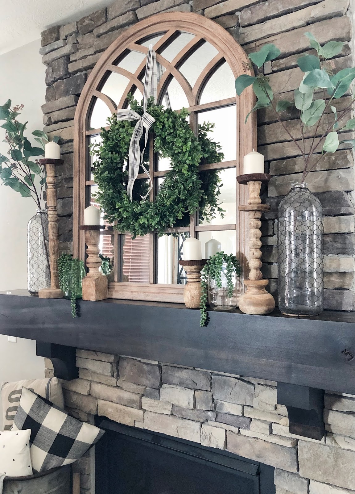 Summer farmhouse styled fireplace, arched mirror, wood candle sticks, glass vases with faux greenery, boxwood wreath